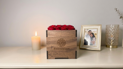 Red preserved roses in an engraved walnut box beside a candle and framed photograph.